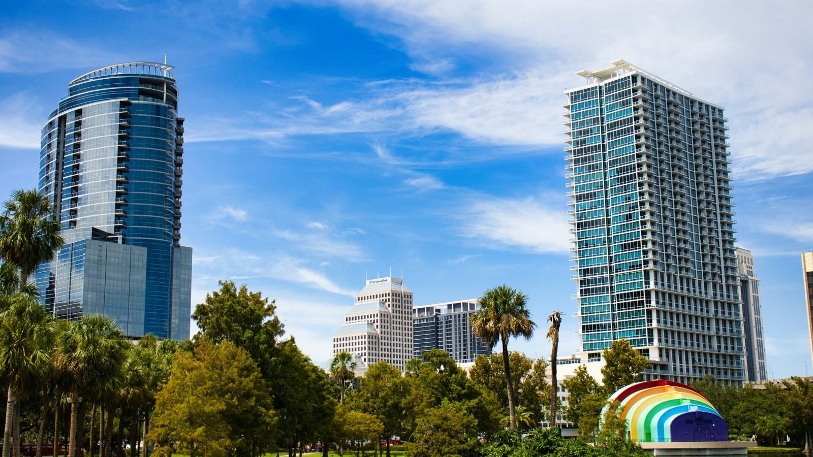 Torres residenciais à beira do lago Eola, no centro de Orlando, com palmeiras e céu azul